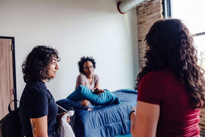 Young Covenant House resident sitting on their bed talking to staff