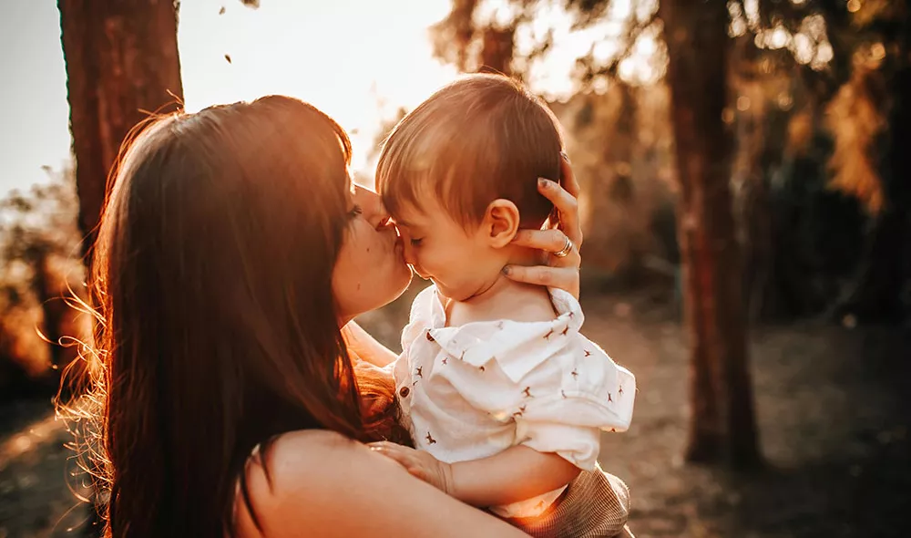 young mother holding and kissing child | Covenant House - Photo by Helena Lopes