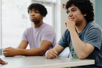 Former homeless teenagers seated at table inside shelter | Covenant House