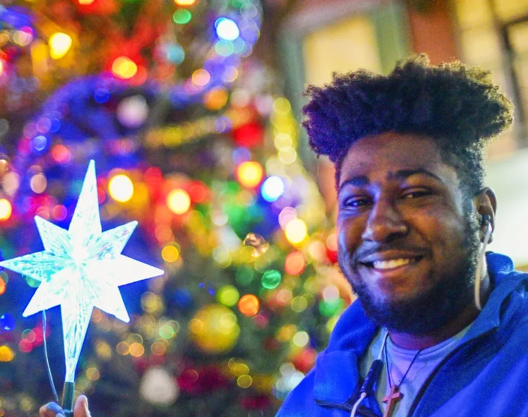12 Days of Giving - Donate Now to Homeless Youth - Former homeless teen standing next to Christmas Tree | Covenant House