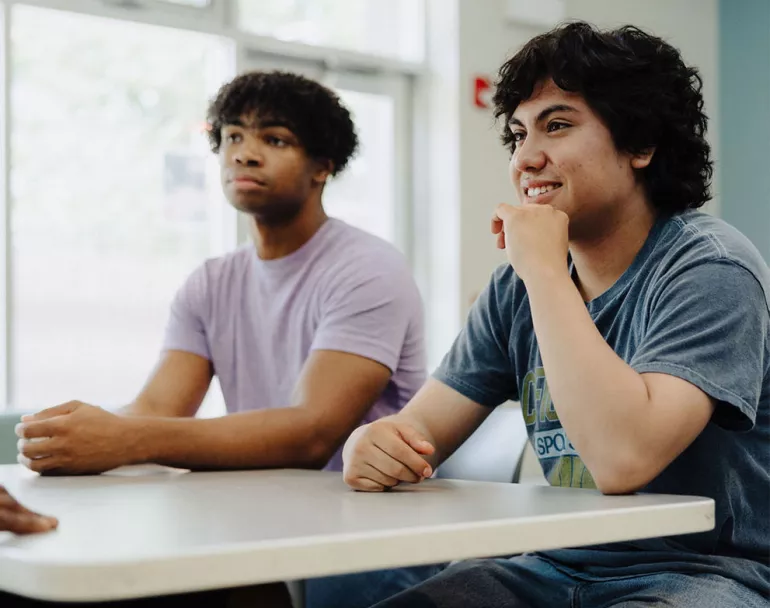 Former homeless teenagers seated at table inside shelter | Covenant House